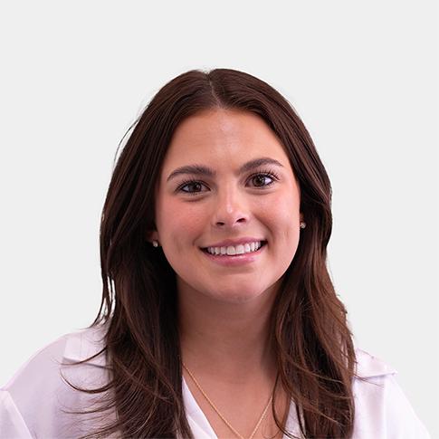 Portrait of a smiling woman with long brown hair wearing a white blouse against a light gray background.
